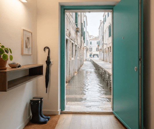 Rain boots and umbrella by a Venetian apartment entrance during acqua alta, wooden passerella visible outside, AQ Digital
