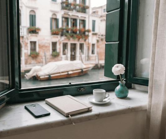 Smartphone face down on a marble windowsill in a restored Venetian apartment, closed notebook, espresso cup and teal vase, canal view, AQ Digital