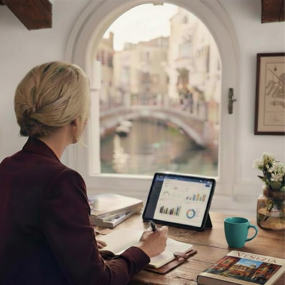 AQ Digital founder working at a Venetian arched window overlooking a canal, tablet open to the welcome book dashboard